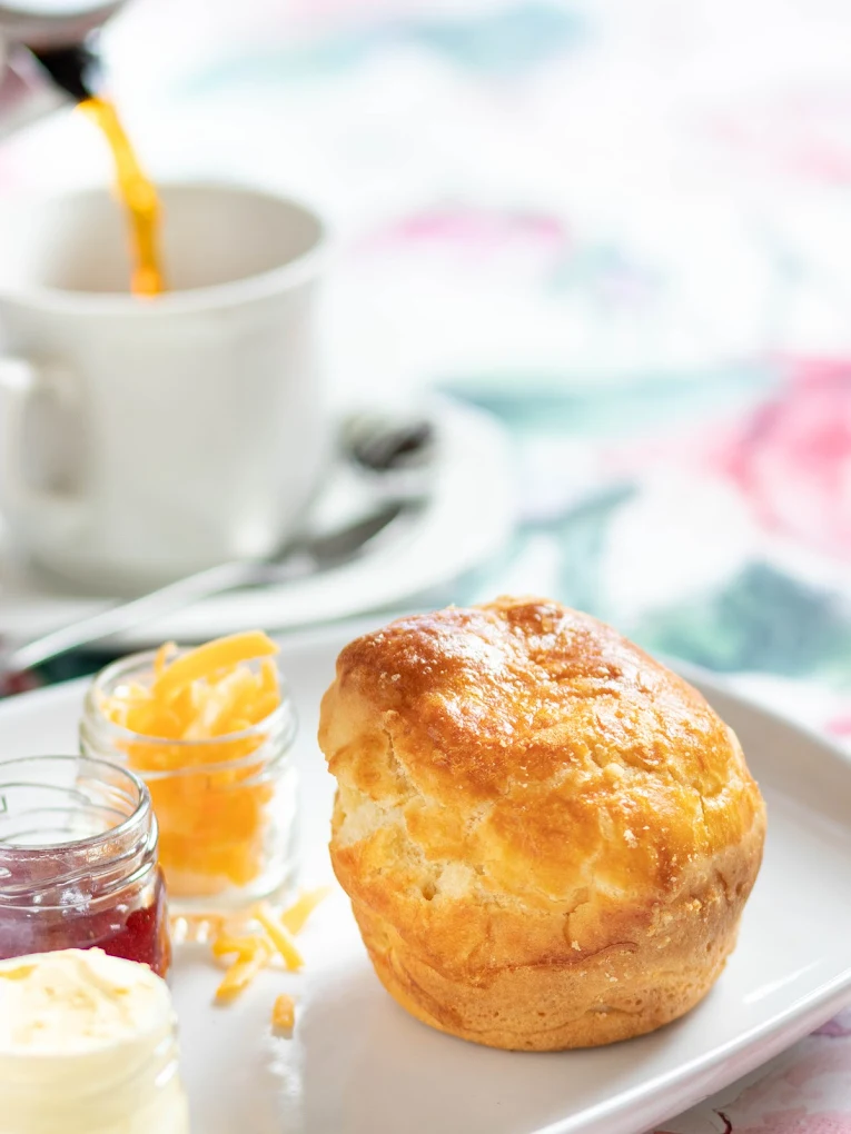 A freshly baked scone served with cheese, jam and a cup of coffee